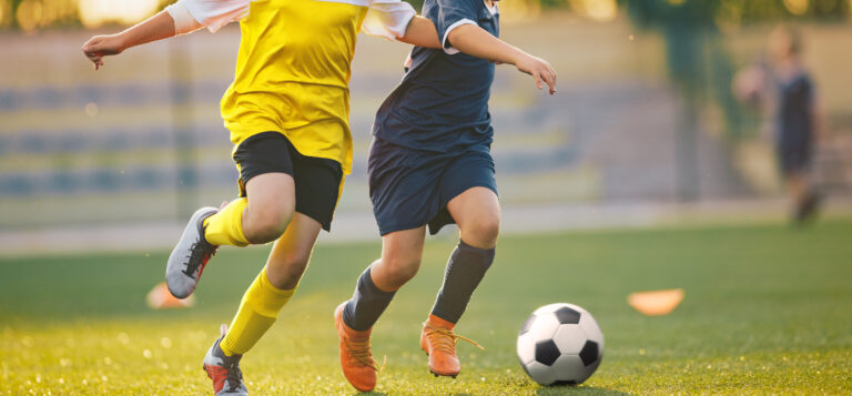 Two Soccer Players in a Duel on Grass Venue. Boys Running After Black and White Soccer Ball. Kids in Soccer Jersey Kits