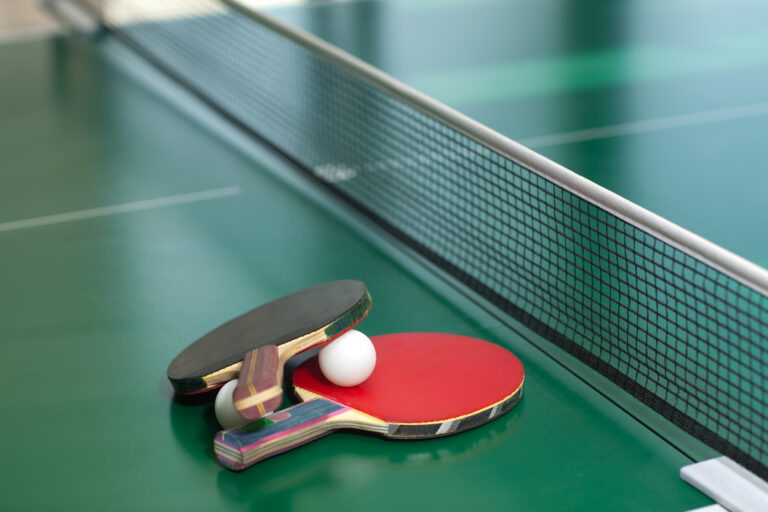 Two table tennis or ping pong rackets and balls on a green table with net